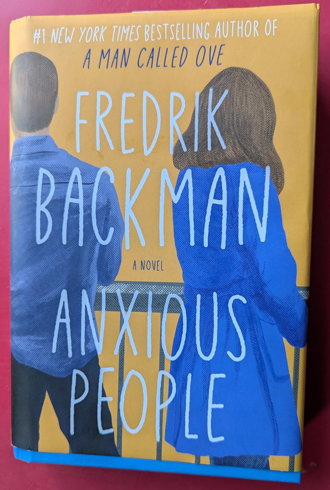 A hardback of Anxious People by Fredrik Backman on a red cloth